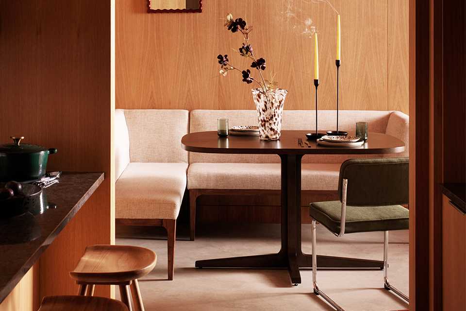 Wooden dining room with cosy lighting to set the scene and cream corner sofa with dining table in front of it with a wooden bar in corner.