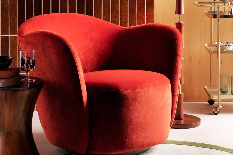 Orange velvet accent chair in living room cosy corner with wooden floor lamp with white shade and wooden side table with marble top.