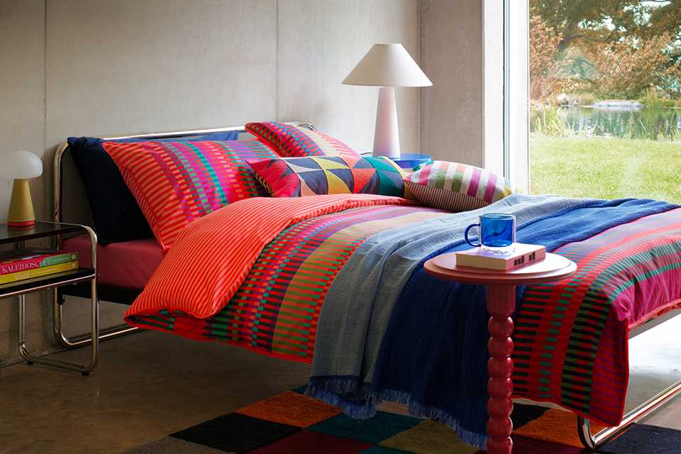 colourful bold bedroom with striped colourful bedding and bobble side table in red and white lamp.