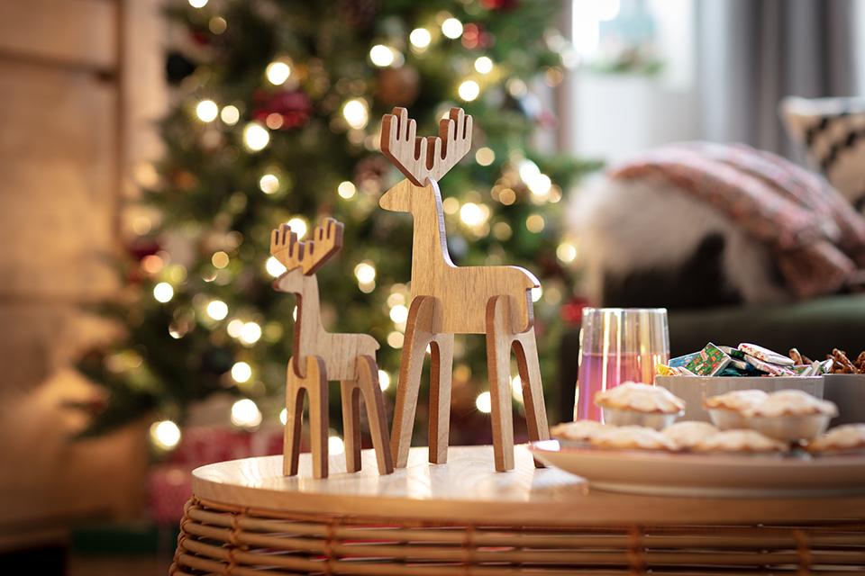Two light wooden reindeer ornaments sat next to mince pies with a Christmas tree in the background.