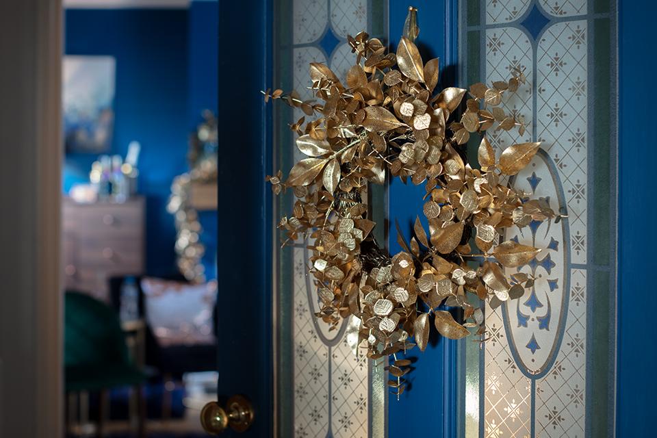 A gold foliage Christmas wreath on a blue front door.