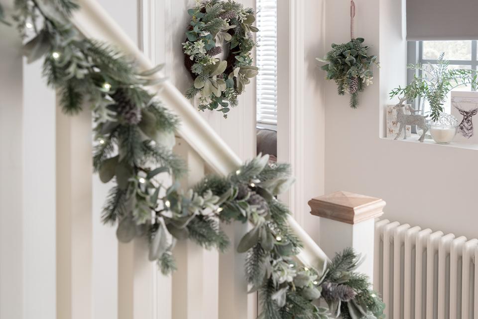 A frosted green foliage garland running down a banister, with matching wreaths on the wall.