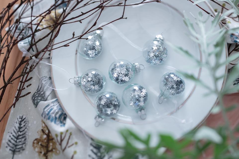 Clear baubles with loose sparkly silver stars inside placed on a white dinner plate.