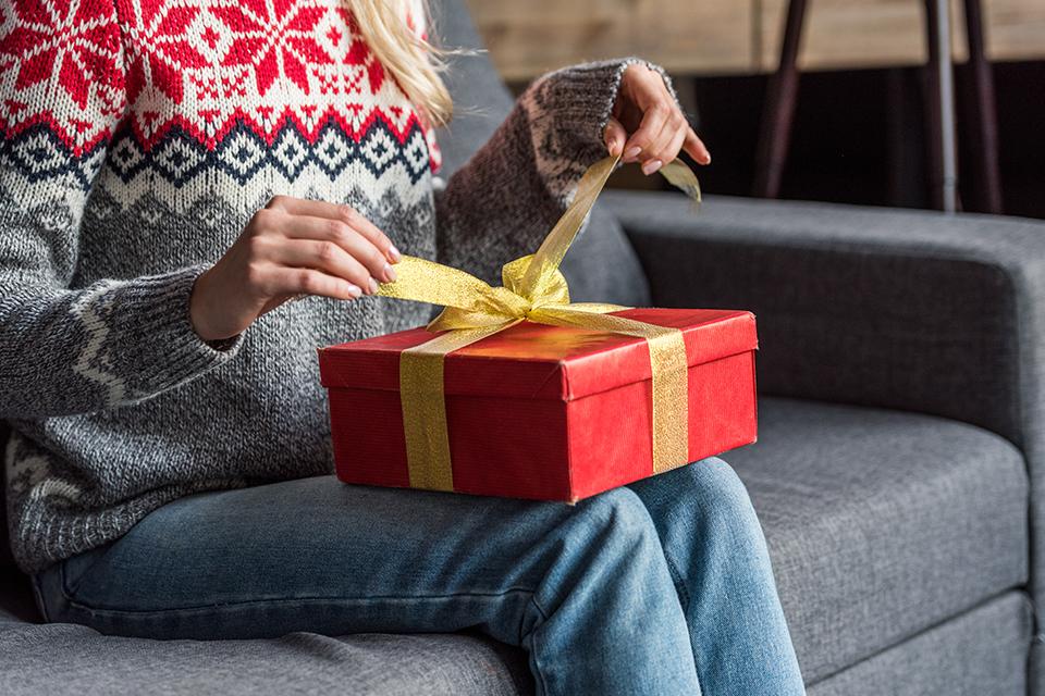 Woman in Christmas jumper opening present at home.