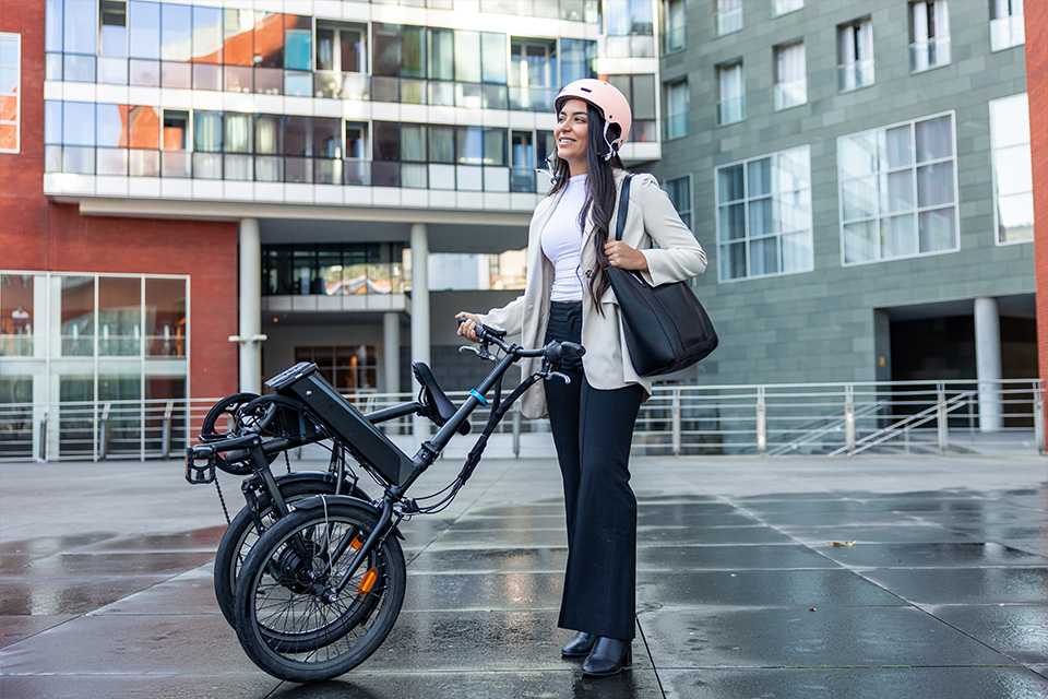 A girl in a helmet and formal wear standing next to her folding bike.