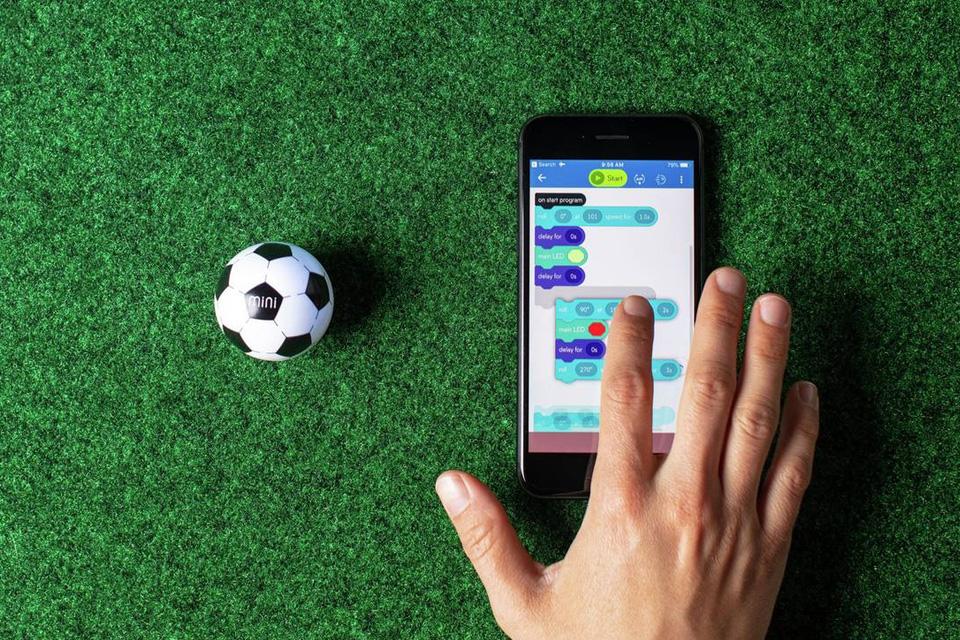 A hand on a smartphone coding instructions to a football Sphero.