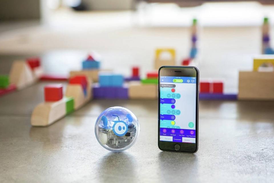 A Sphero codable robot next to a smartphone showing a coding app.