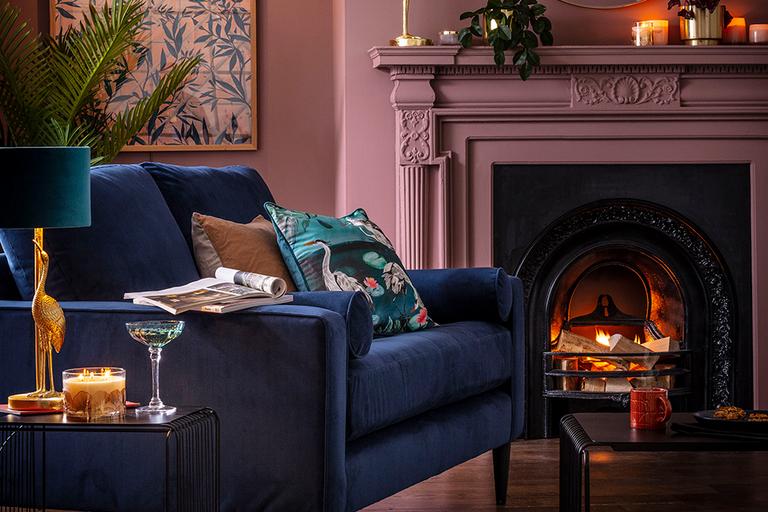 Image of a navy velet sofa in a dusky pink living room by a fire.