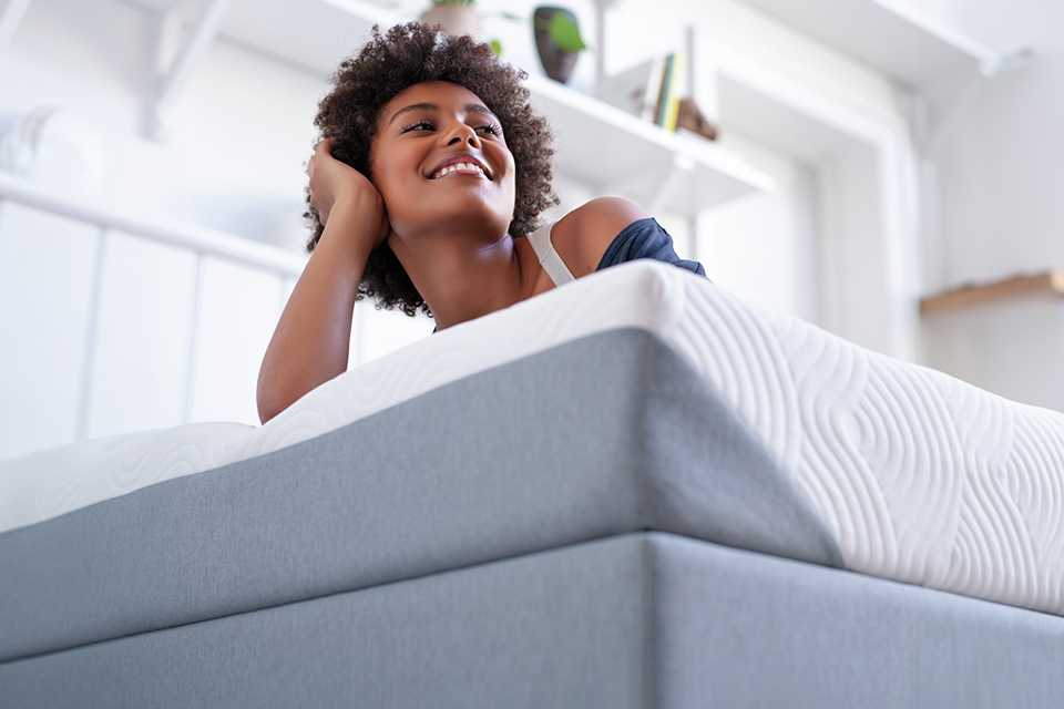 Woman lying on mattress in bedroom.