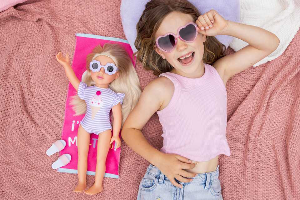 Girl lying on blanket with sunglasses on posing with her 18 inch DesignAfriend doll.