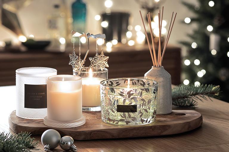 Image of four festive candles and a reed diffuser on wooden table.