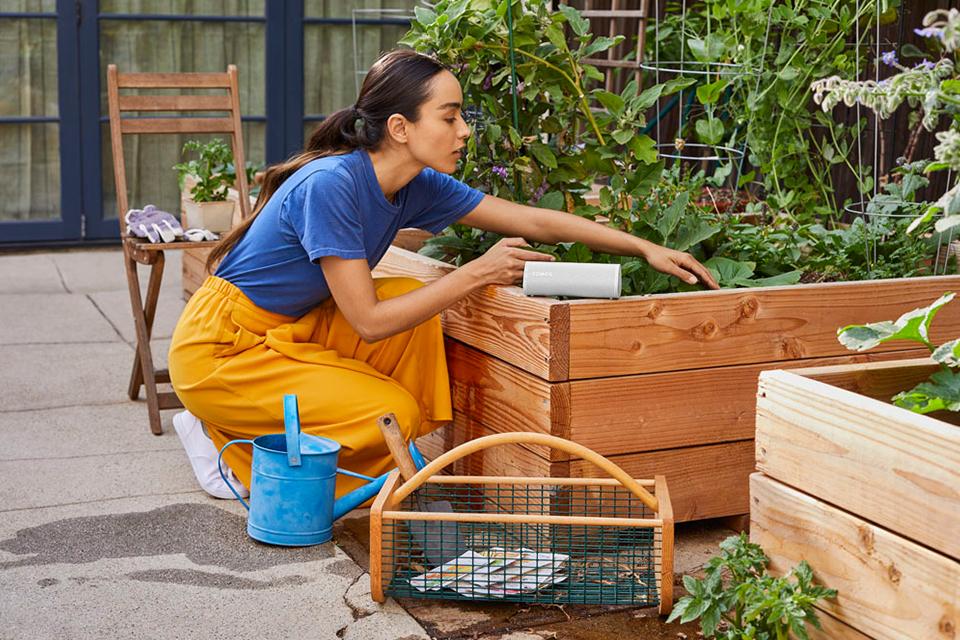 A woman is shown gardening with a Sonos speaker next to her.