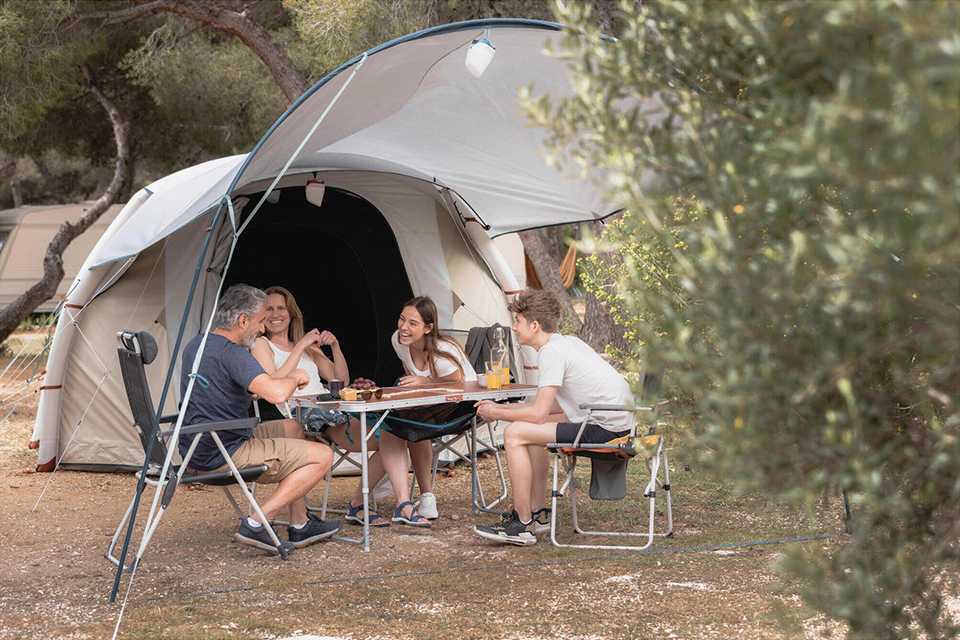 A family of 4 sitting outside their tent on a folding camping dining table set.