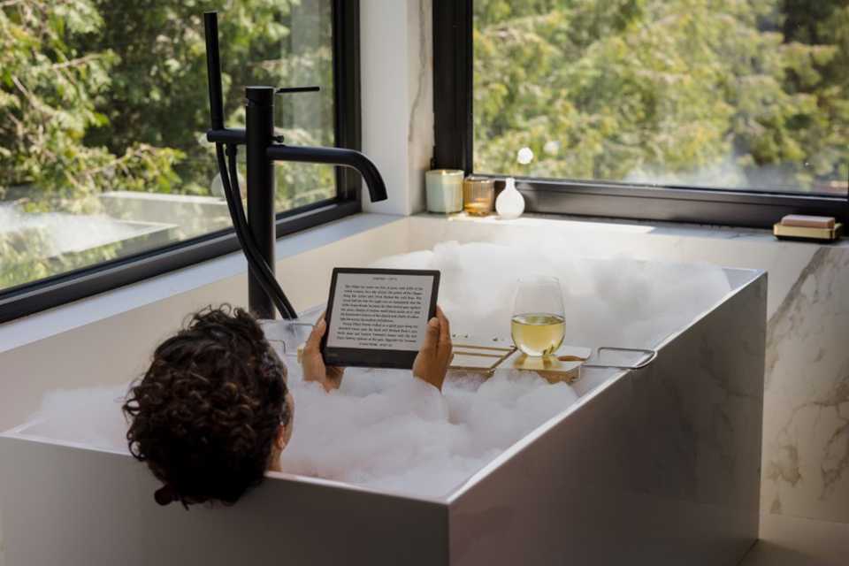 A person reading on a Rakuten Kobo eReader while in a bubble bathtub.
