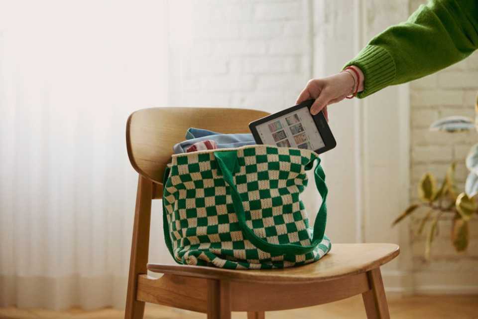Hand placing a compact Rakuten Kobo eReader into a green checkered tote bag.