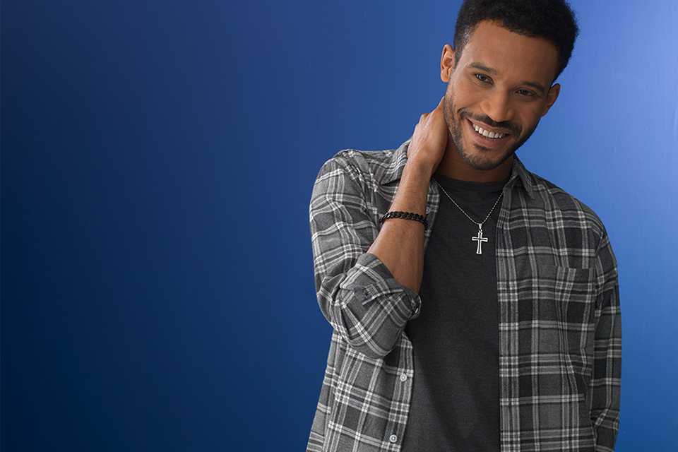A man in a grey check shirt wearing a Revere silver crucifix pendant necklace.