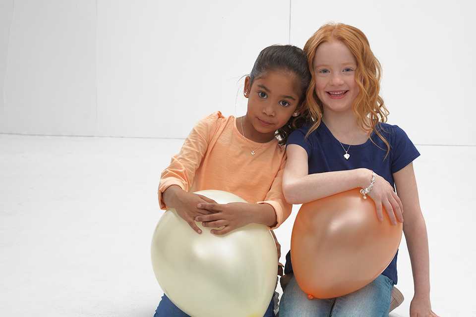 Two girls sitting with balloons on their laps wearing Revere sterling silver pendant necklaces.