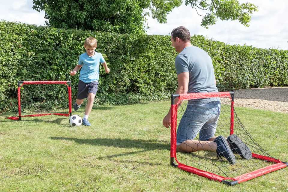 A kid playing football with his dad in a garden.