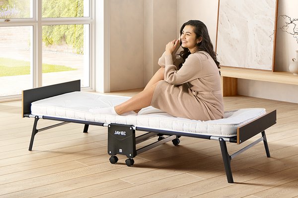 A woman sitting on Jay-Be® Grand folding single bed with e-Pocket™ mattress in a bedroom setup.