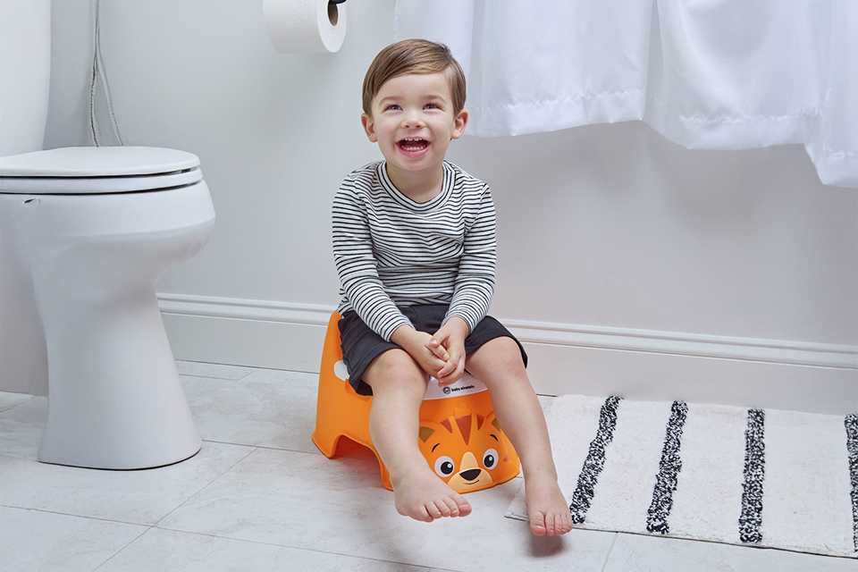 A toddler sitting on an orange baby Einstein tiger potty.
