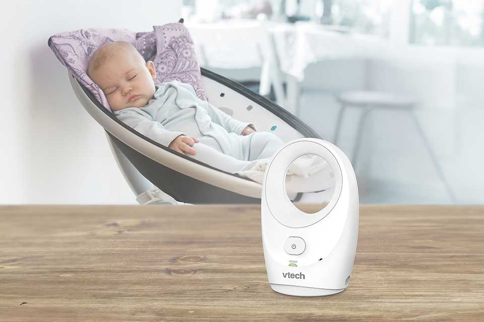 A Vtech DM1111 Audio Baby Monitor on a table next to a sleeping baby.