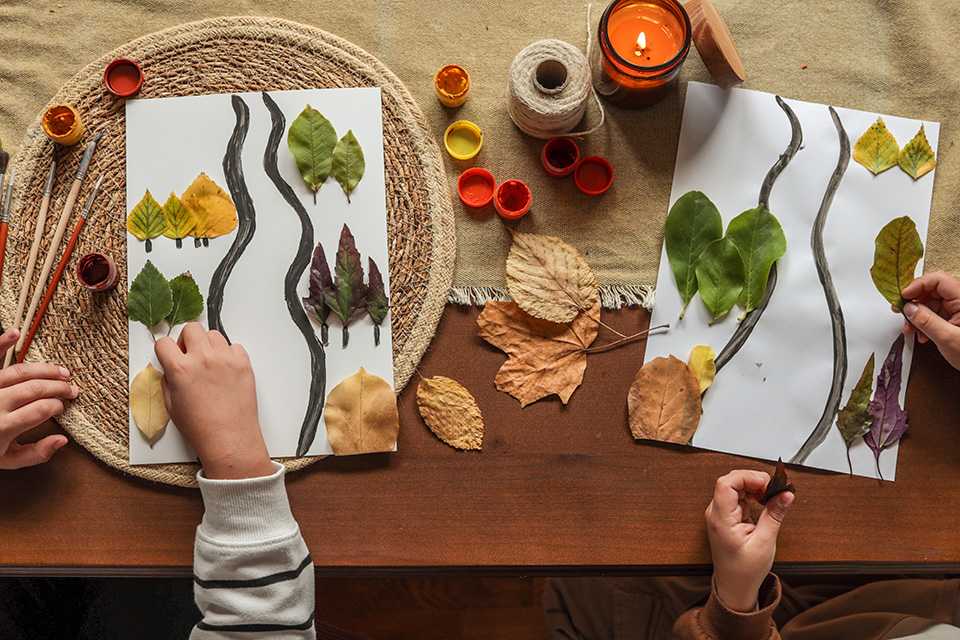 A kid making a nature-inspired collage by sticking leaves on a paper.