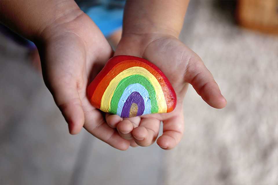 A collage of a pebble painted in rainbow colours and a child painting a stone.