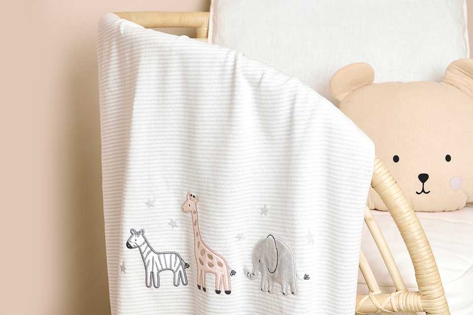 A JOJO MAMAN BÉBÉ welcome little one embroidered baby blanket on a chair.