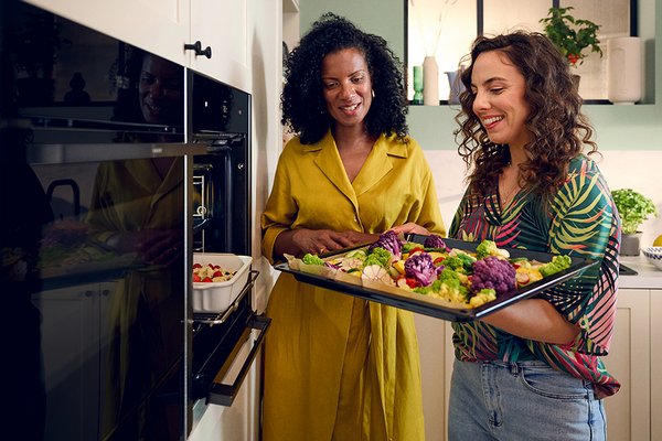 Two women standing in front of an oven with a tray of food.