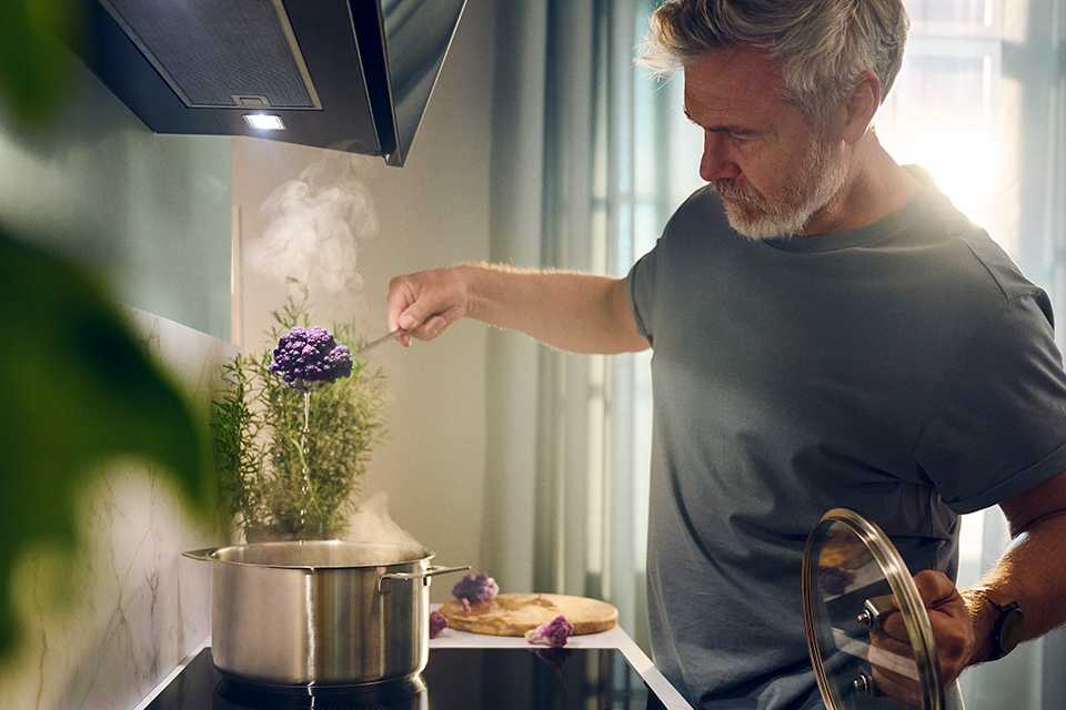 A man cooking over a kitchen counter with vapours rising from a vessel.