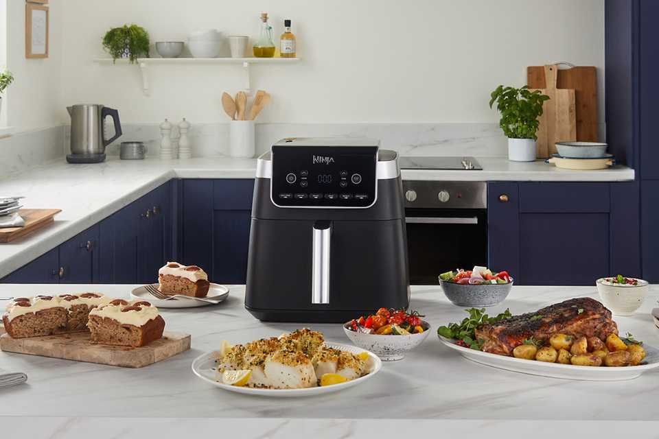 Ninja MAX PRO AF180UK 6.2L Air Fryer in black colour placed in a kitchen with multiple dishes around it.