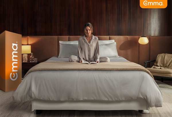 A woman sitting on bed with Emma box packaging beside.