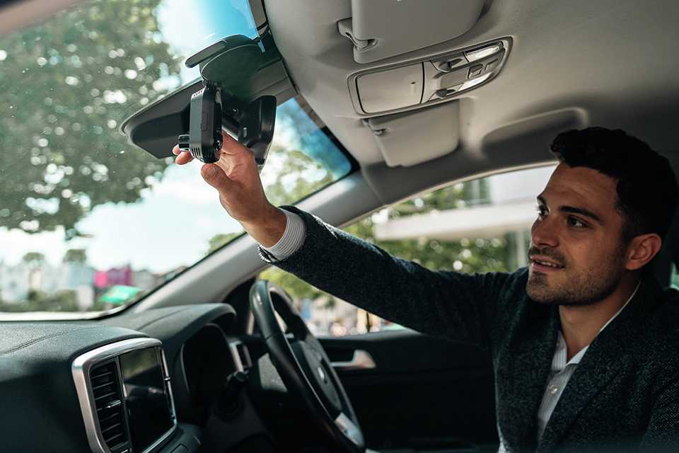 A man attaching Nextbase IQ 1440P Smart dash cam to the rear view mirror of his car.