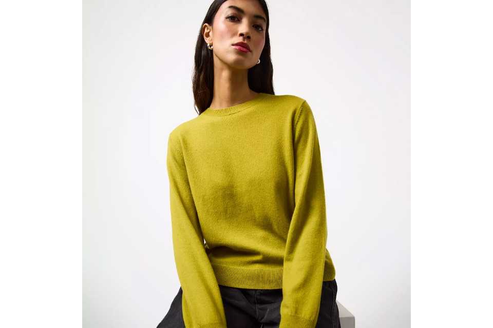 Person wearing a bright yellow long-sleeve crew-neck sweater paired with dark grey jeans, seated on a light-colored surface.