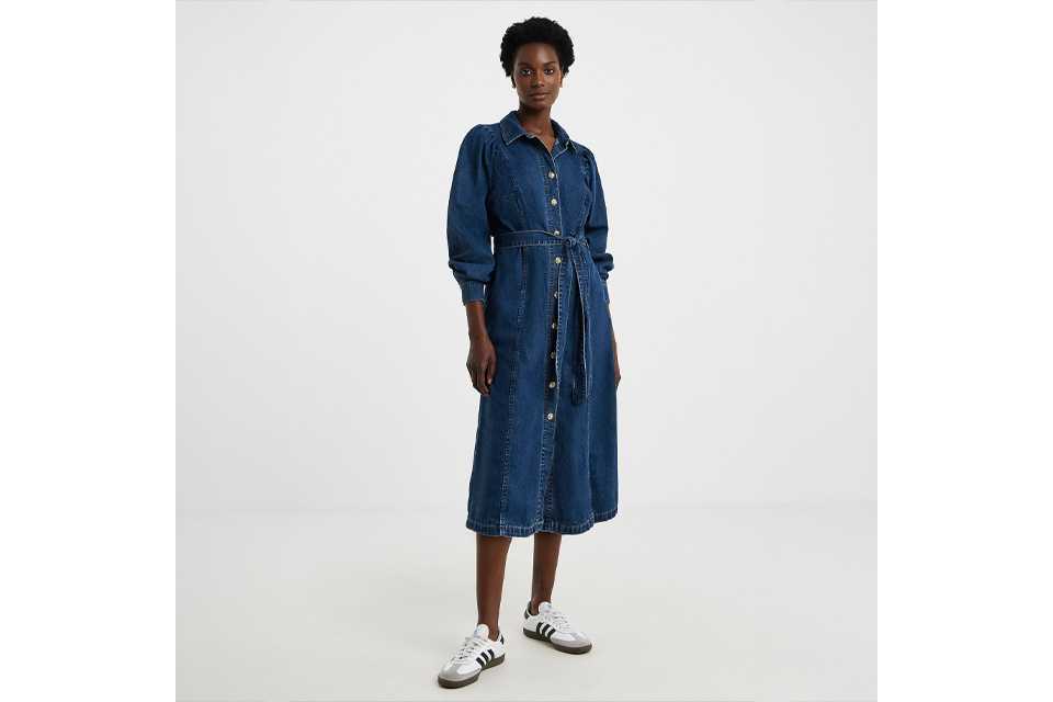 Person wearing a long-sleeve button-down denim midi dress with a matching tie belt at the waist, styled with white and black sneakers.