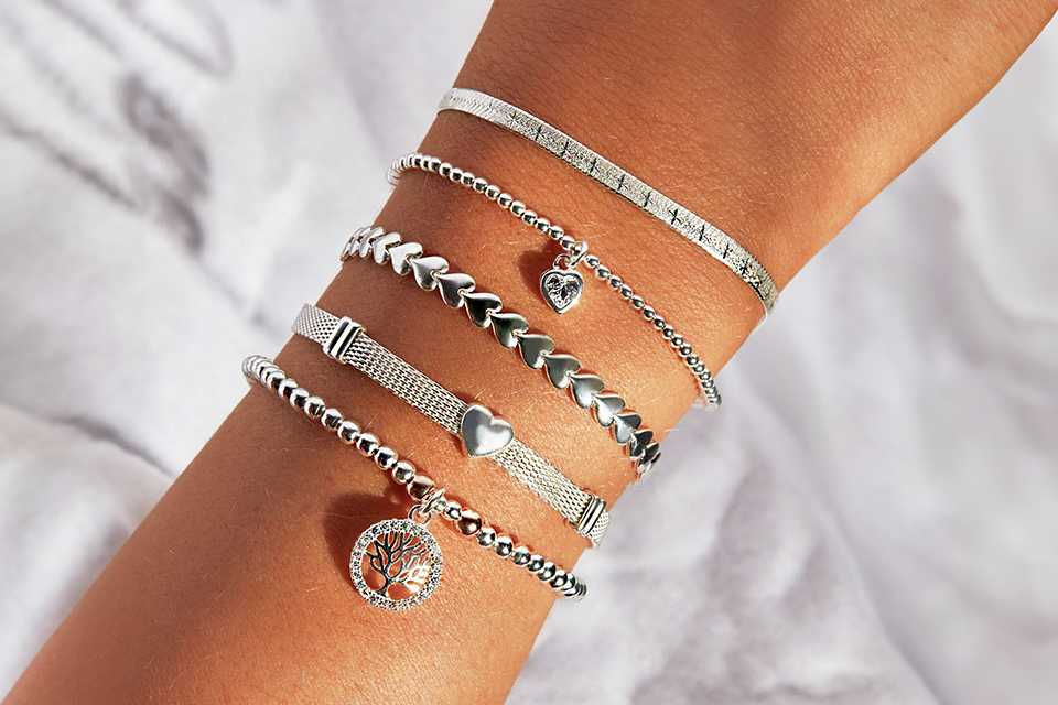 Five silver bracelets, including some with charms, on a person's hand.