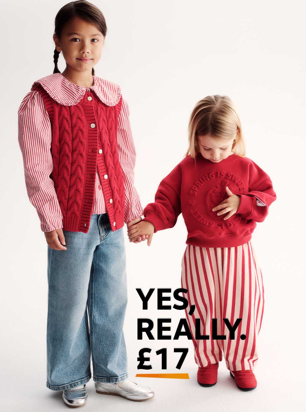 Person standing and holding hands with someone partially visible, wearing a red and white striped shirt with a large collar, a red cable-knit buttoned vest, light blue wide-leg jeans, and silver shoes. The background is plain and light-colored.