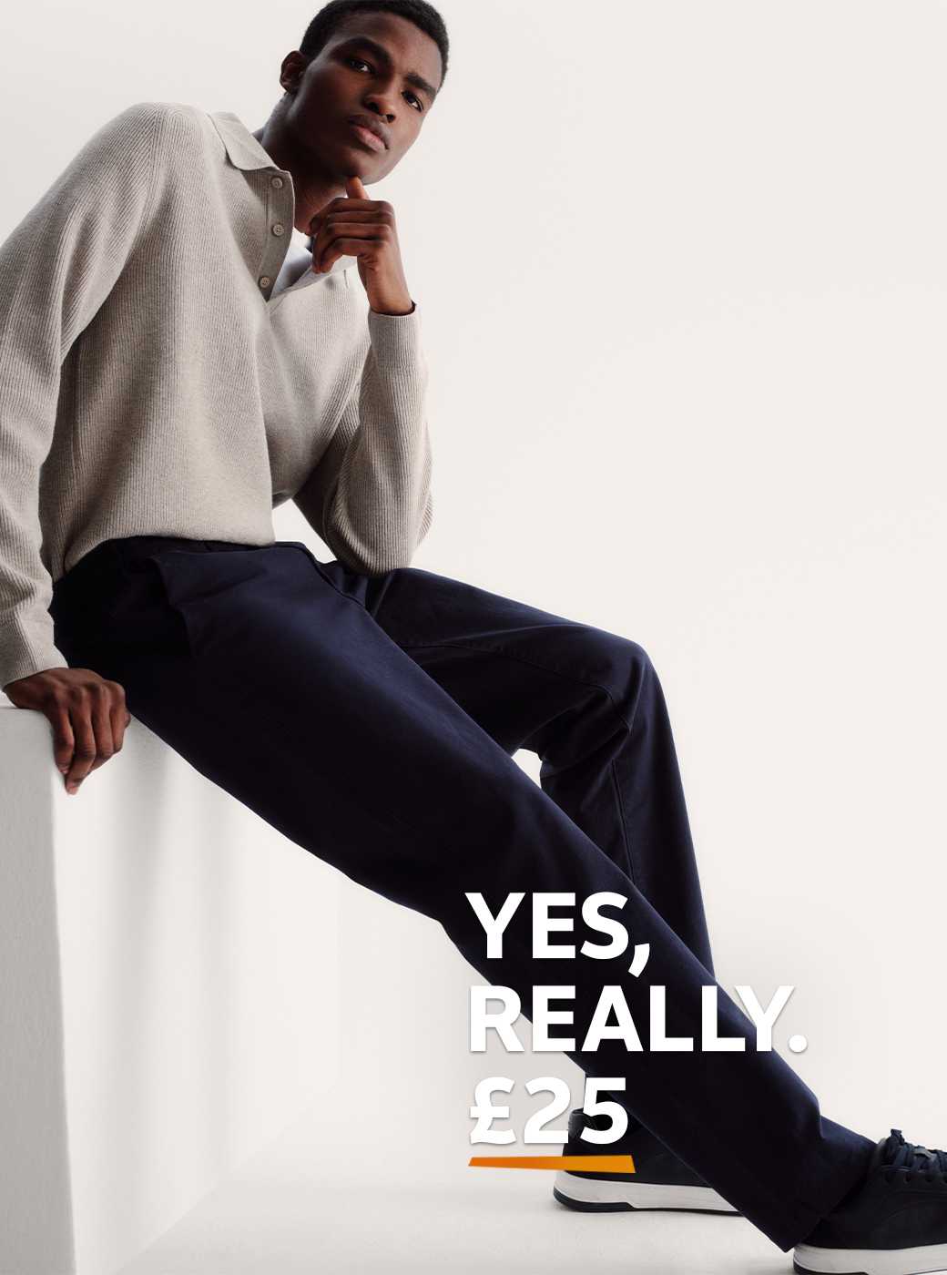 A man wearing navy chinos, with trainers and a neutral jumper.