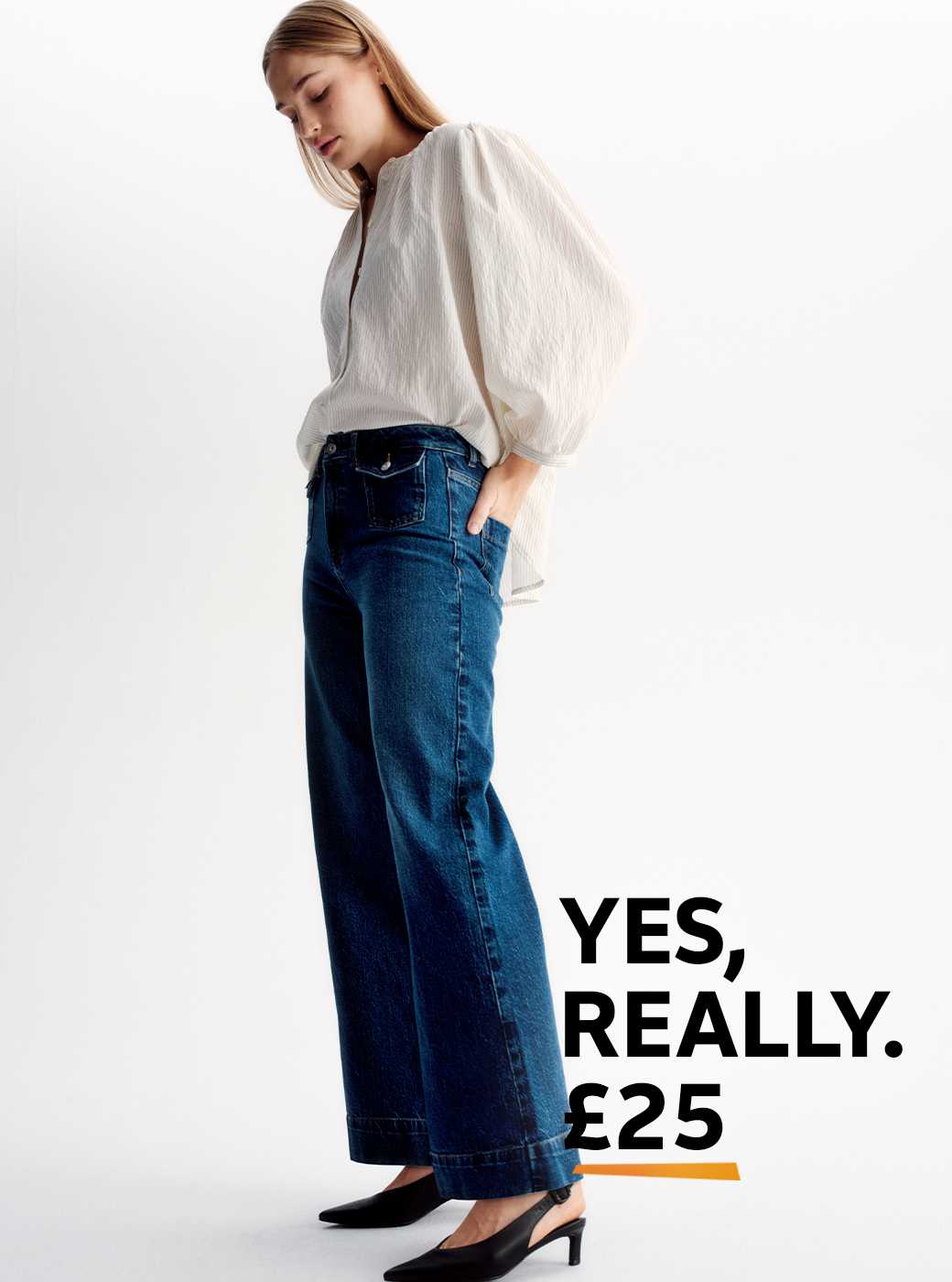 A woman wearing relaxed flare jeans, with a neutral blouse and black shoes.