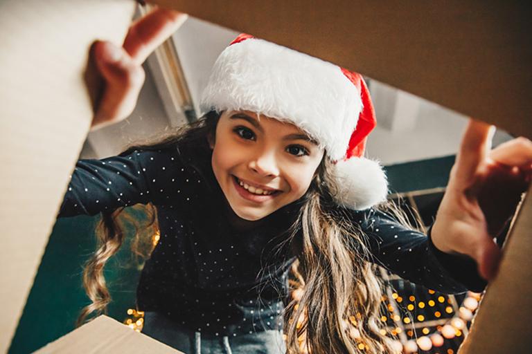 A girl wearing a santa hat looking into a present.