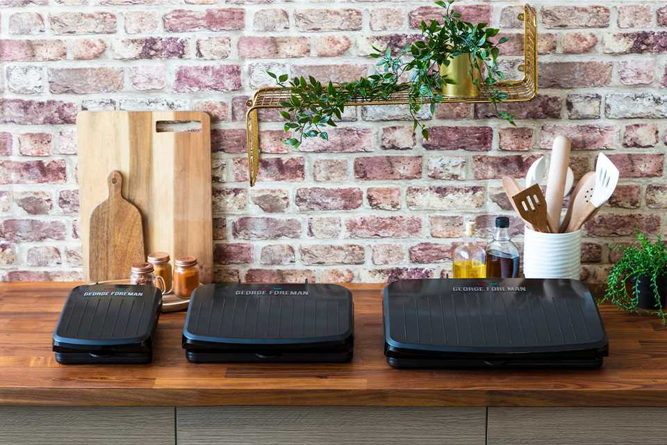 Three George Foreman fit grills on a wooden counter.