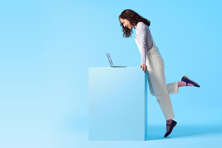 A woman stands at a desk looking at a laptop screen.
