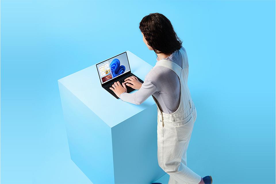 Young woman stands at a desk looking at a laptop screen.
