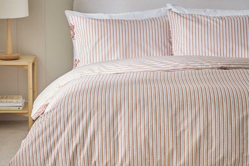 Stripe bedding on cream headboard in bedroom.