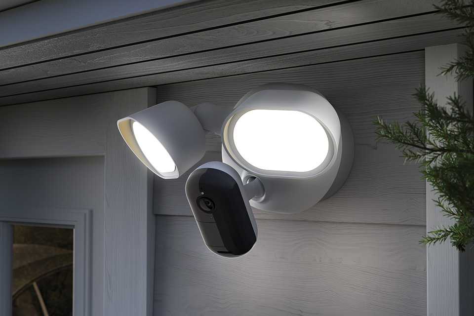 A pair of Arlo wired floodlight placed outside a home and switched on.