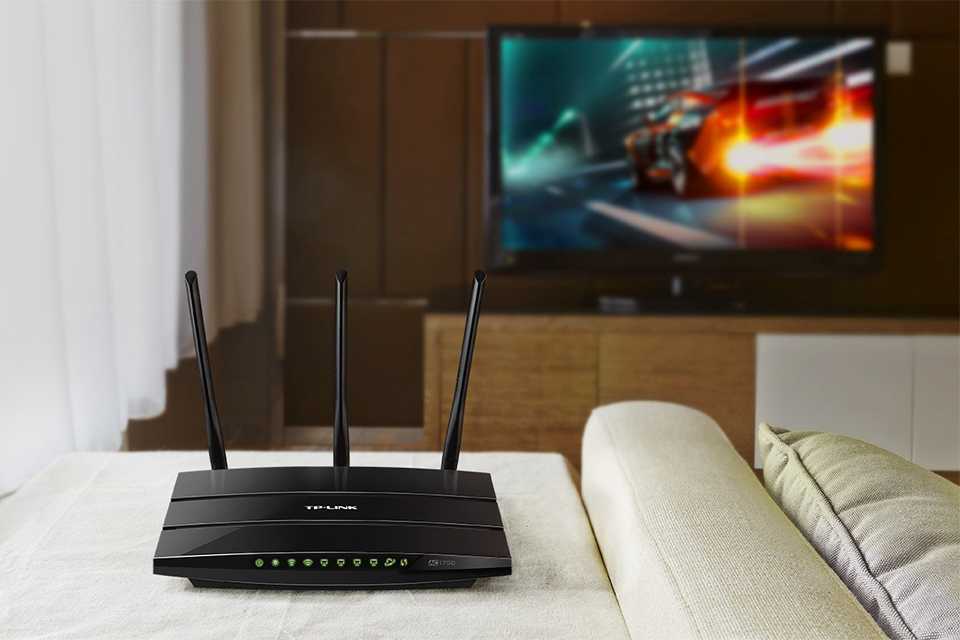 A black TP link wireless WiFi router placed next to a sofa in a living room.