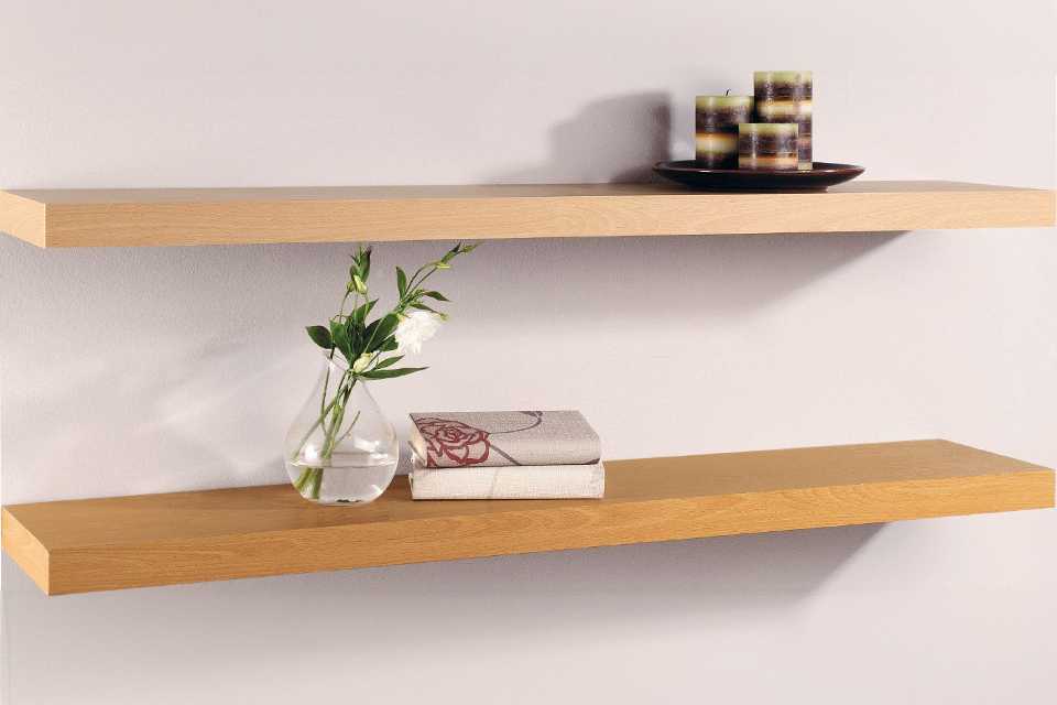 A pair of wooden shelves with a vase, books and candles on it.