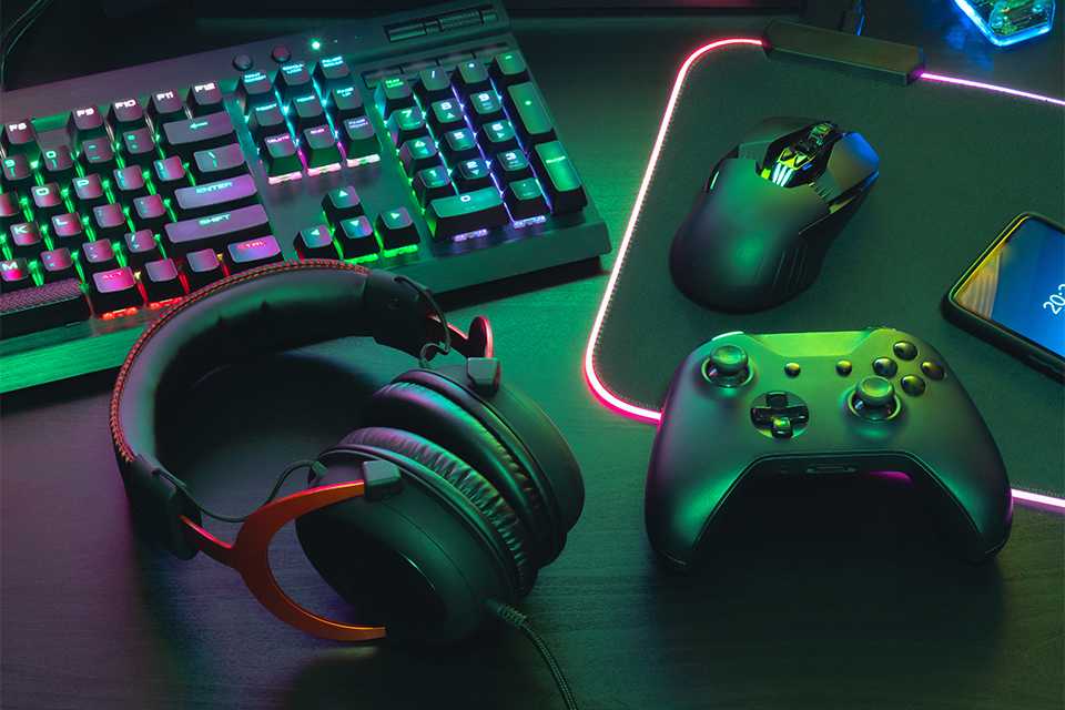 An assortment of tech and gaming accessories including a keyboard, a headset, a video game controller and more.