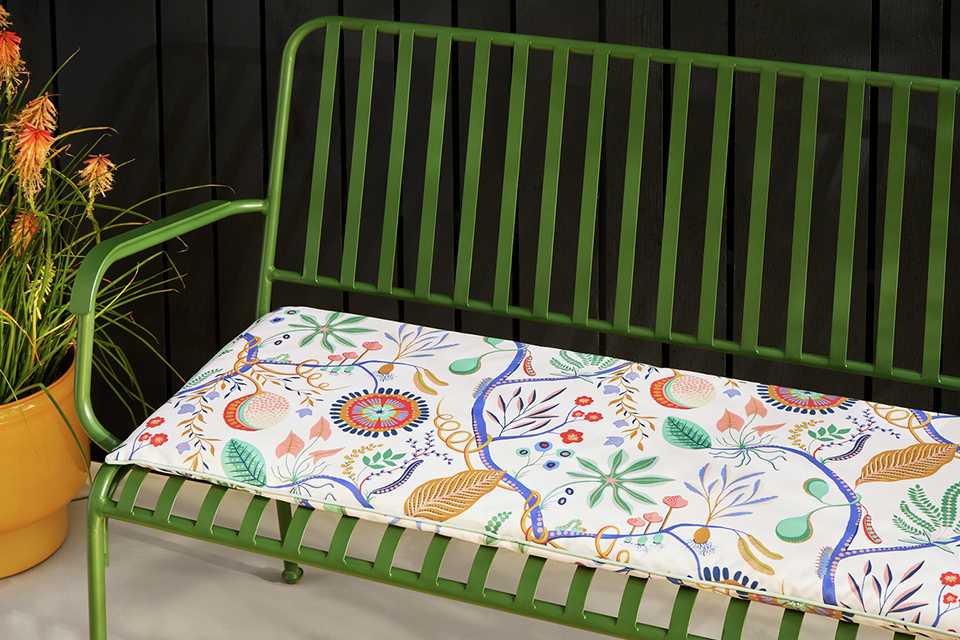 Green wire garden bench with floral seat cushion.