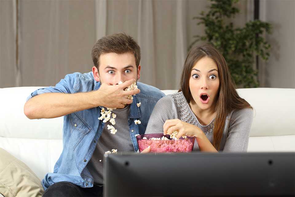 Two people eating popcorn, watching a movie.